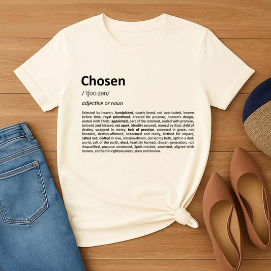 Cream t-shirt with 'Chosen' definition text on a wooden surface with jeans and shoes.