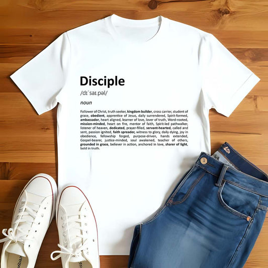 White t-shirt with 'Disciple' definition text, white sneakers, and blue jeans on a wooden floor.