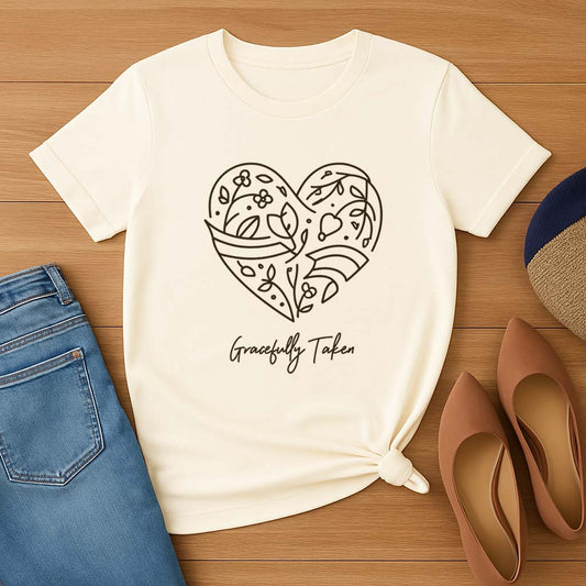 White t-shirt with heart design and 'Gracefully Taken' text on a wooden surface with jeans and shoes.