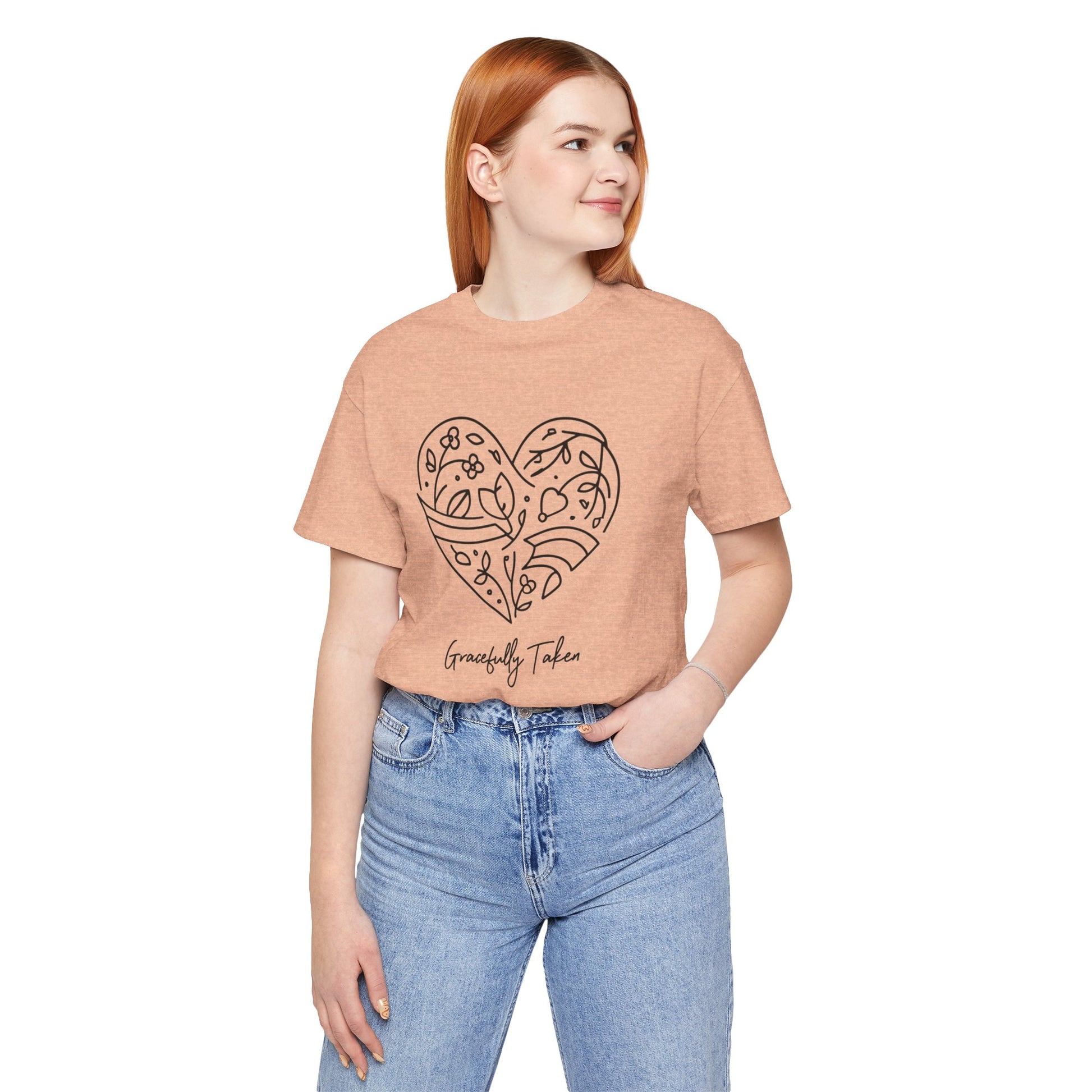 Person wearing a peach t-shirt with a heart design and text, standing against a white background