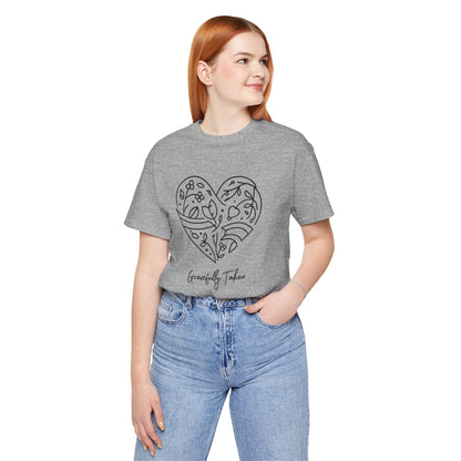 Person wearing a gray t-shirt with a heart design and text, standing against a white background