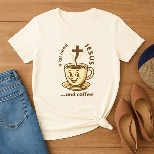 Cream t-shirt with a coffee cup graphic and text on a wooden surface with jeans and shoes.