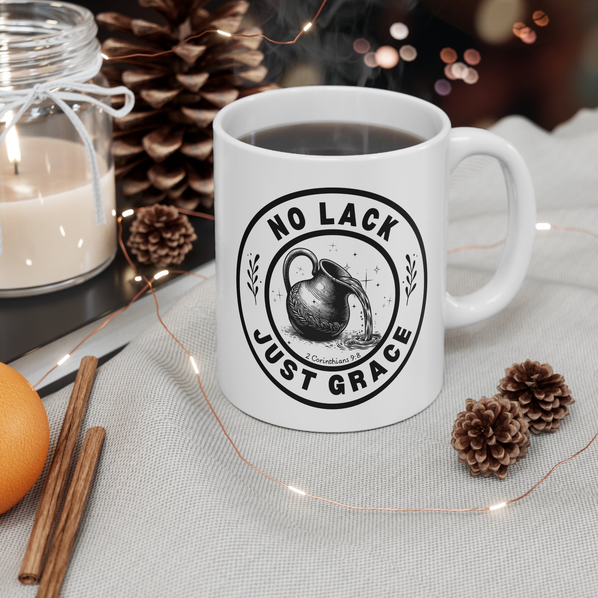 White mug with 'No Lack Just Grace' design on a table with candles and pinecones.