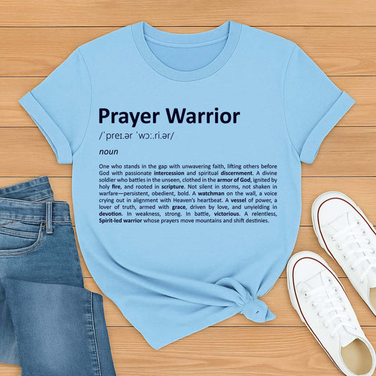 Light blue t-shirt with 'Prayer Warrior' definition text on a wooden surface with jeans and shoes.