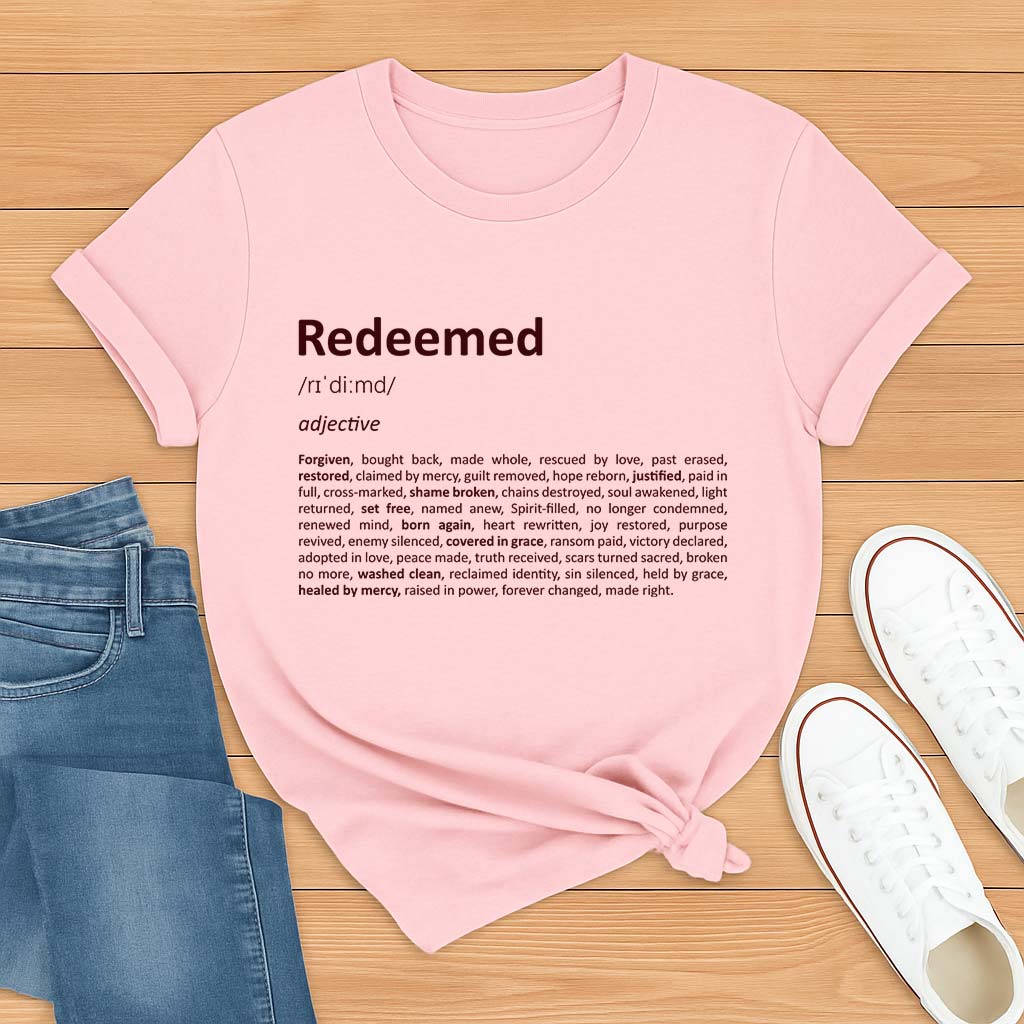 Pink t-shirt with 'Redeemed' definition text on a wooden surface with jeans and shoes.