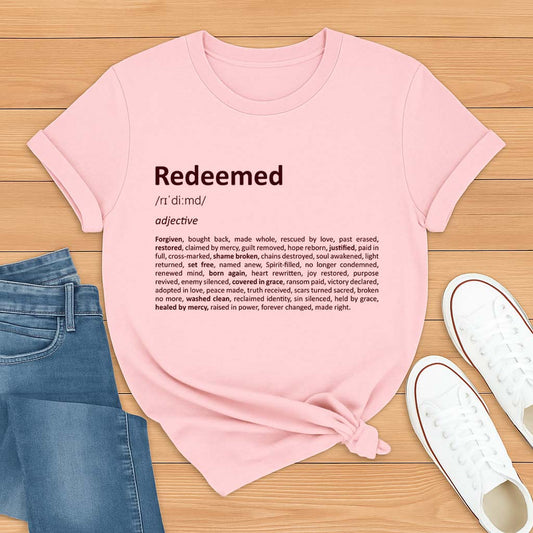Pink t-shirt with 'Redeemed' definition text on a wooden surface with jeans and shoes.