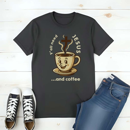 Black t-shirt with a graphic design featuring a coffee cup and text, placed on a wooden surface with shoes and jeans.